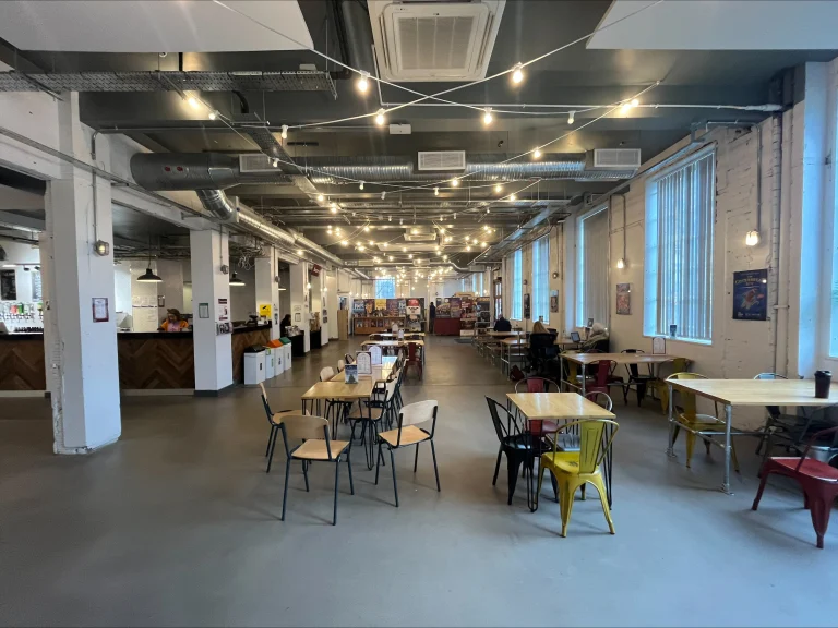 Large open-plan cafe at the Albany Theatre in Coventry featuring flexible hot desks, industrial decor, and bright window seating for freelancers