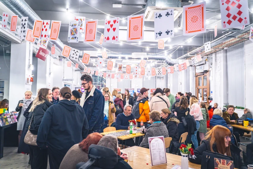 Visitors enjoying the café and bar at Albany Palace Theatre in Coventry, with hanging playing-card decorations, drinks and a lively pre-show atmosphere in the foyer.